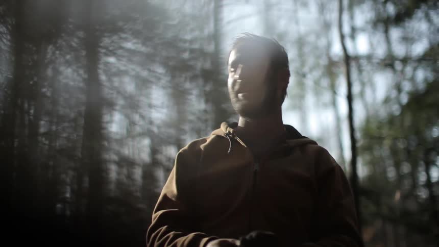 A man removes his hat in the woods