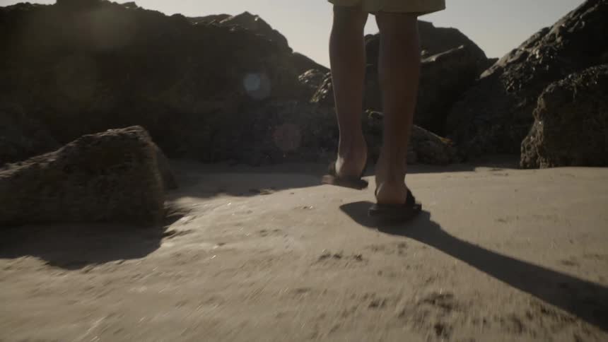Man in flip flops walking up rocky beach