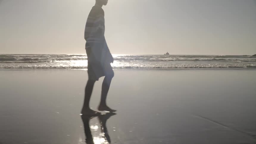 A boy walks along the beach near the water at sunrise