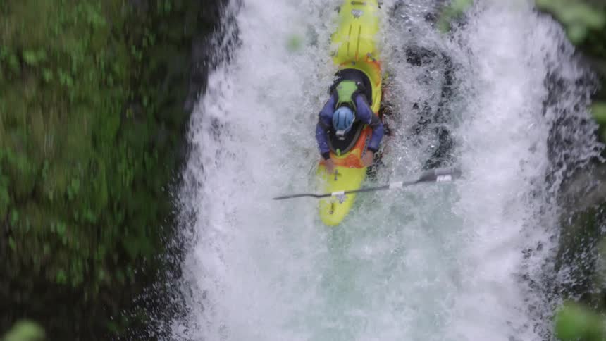 Tight real time shot of a whitewater kayaker dropping off a hundred foot waterfall and tossing their paddle as they descend the drop
