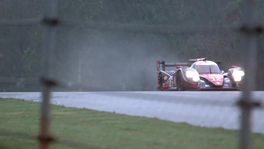 Race cars behind a fence come down the road