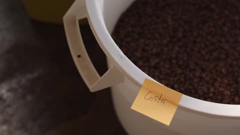 A plastic bowl full on beans, with a sticky note stuck to the bowl that says "costa"