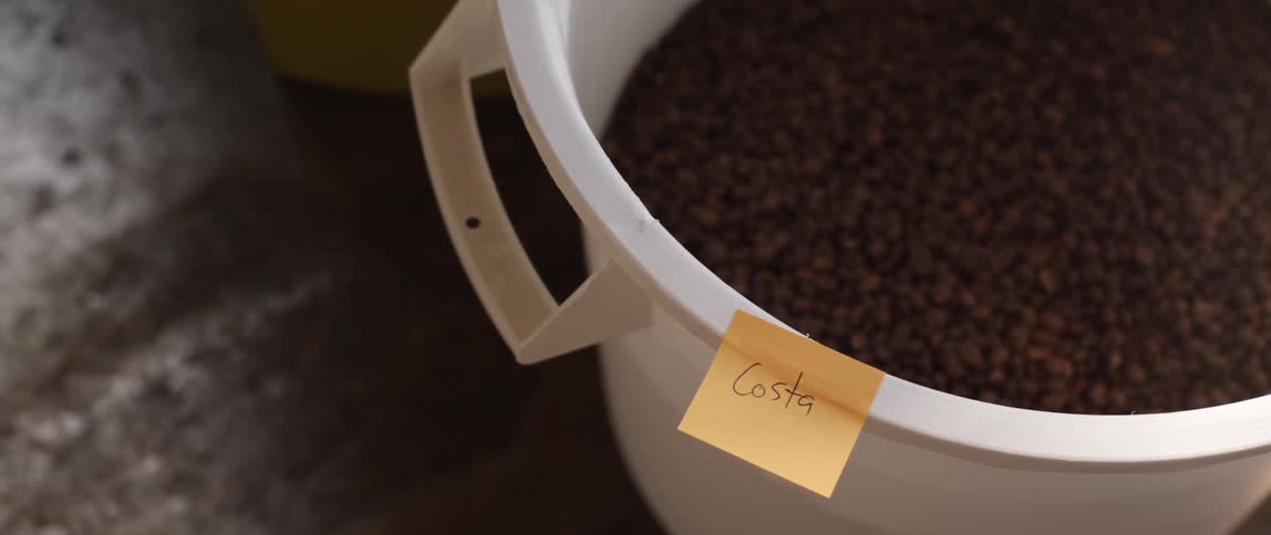 A plastic bowl full on beans, with a sticky note stuck to the bowl that says "costa"