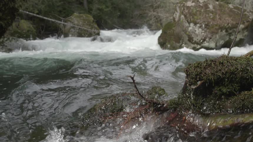 Slow motion hand held shot of clean crisp river water splashing up at the lens of the camera while whitewater rapids are seen in the background