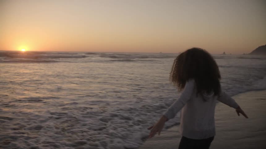 Girl plays in the waves on the beach at sunset