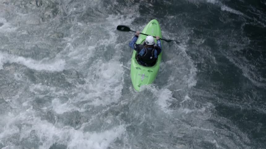 Looking straight down and slowly tilting up showing  a man in a green whitewater kayak paddling through big whitewater