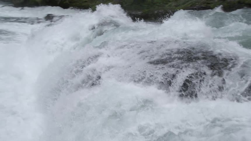 The camera rapidly pans past a whitewater rapid showing off the force and power of this river environment