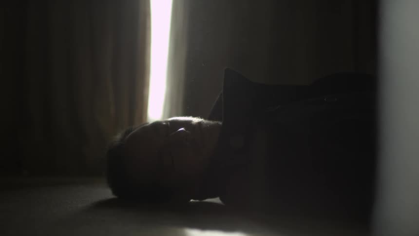 A man laying very still on the floor with his head facing to his right side