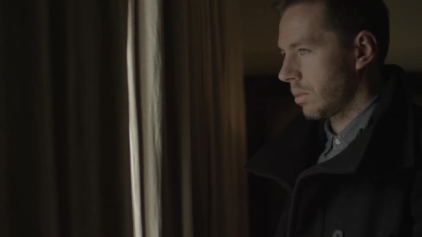 A man opens his eyes and peers through the crack in the curtains