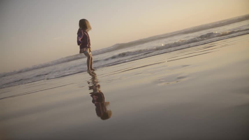 Girl in skirt skips through water on beach edge