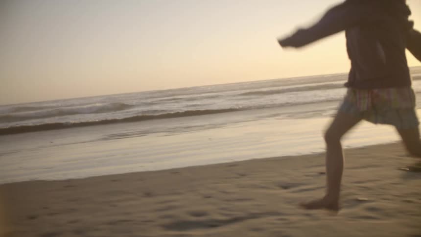 A girl runs on a sandy beach while the sun sets in the background