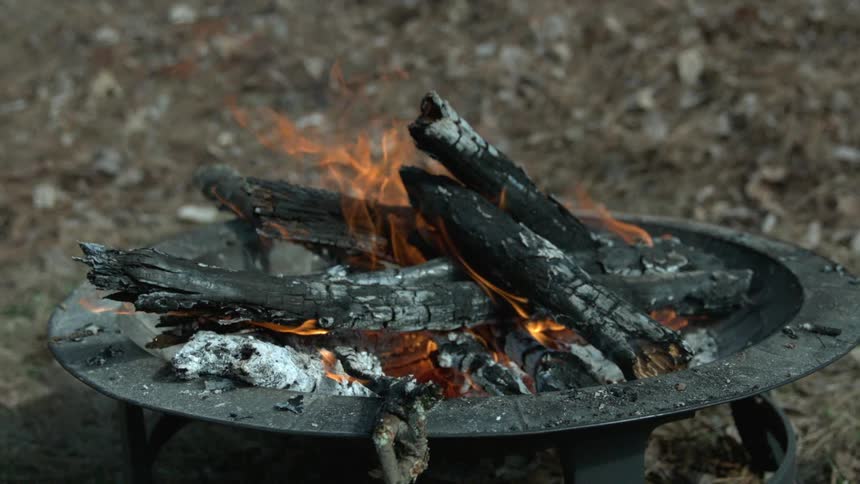 A fire pit with mostly charred logs that are still burning