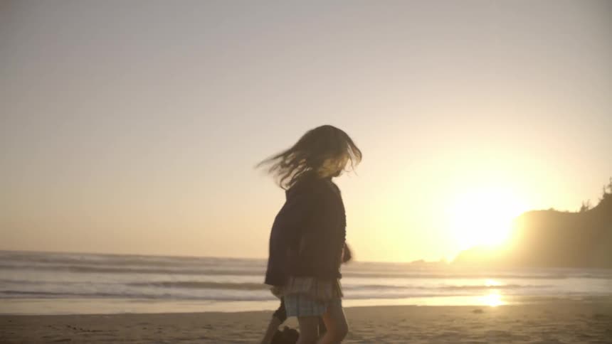 Two children turn in circles on the beach