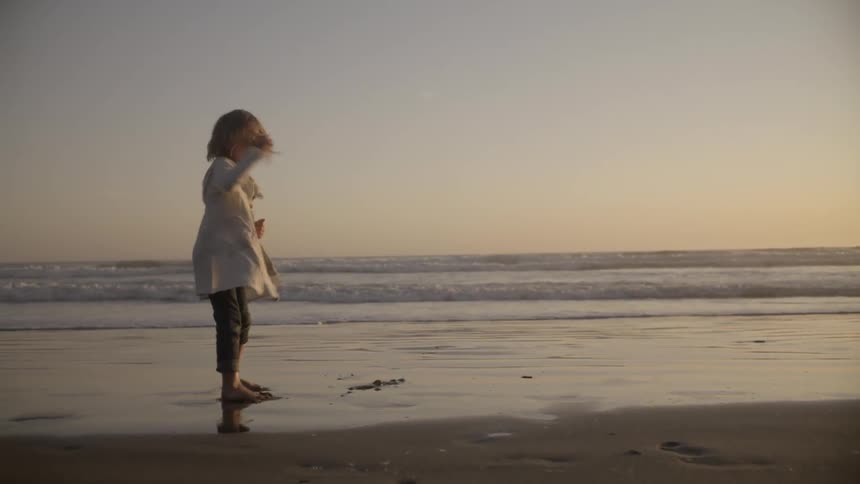 A young girl twirls in circles on the wet sand of a beach