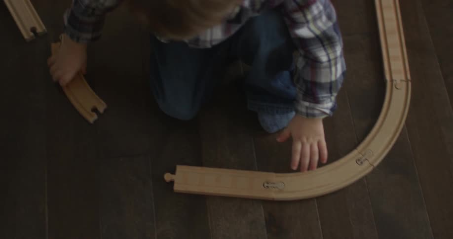 A boy is assembling a toy train track on the floor