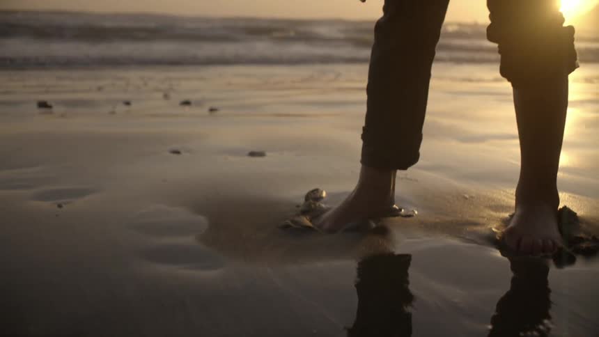 Feet dig into the wet sand of a beach with the sunset in the background