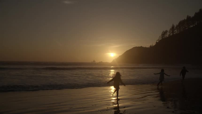 Children run and play on a beach at sunset