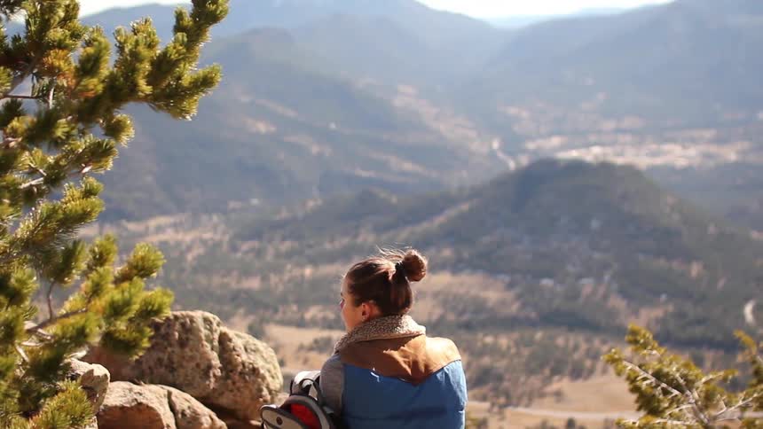 A hiker sits amidst boulders and overlooks a valley