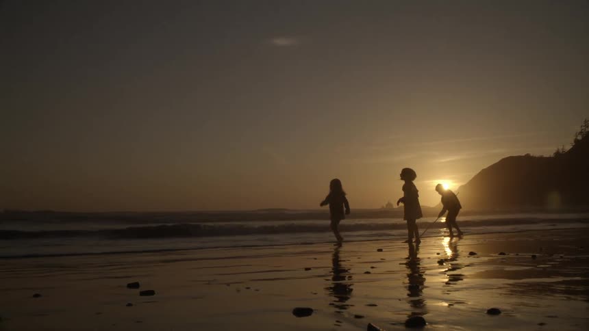 Children play on beach shore at sunset