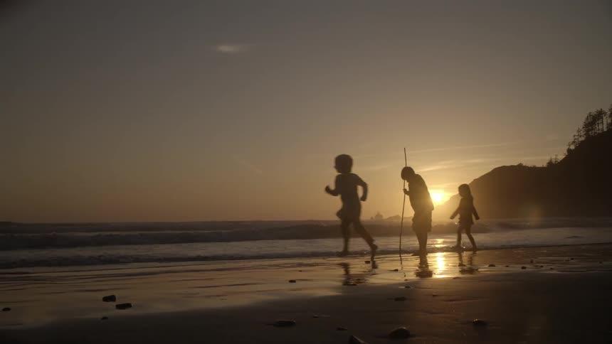A boy is walking along the beach with a stick in his hand when other kids run to join him