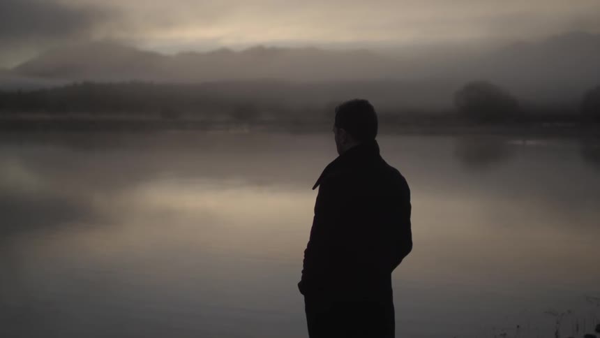 A man looks out over a foggy lake