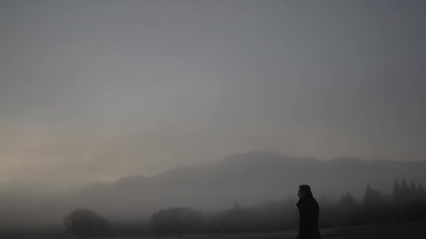 A man standing and looking out over a foggy area with mountains in the background
