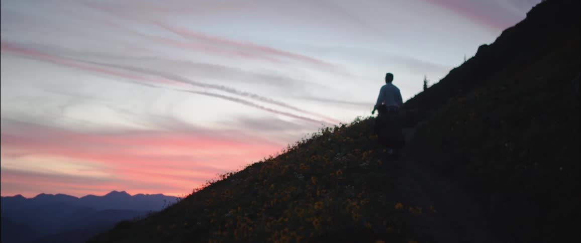 Two men hike up a hill at sunset