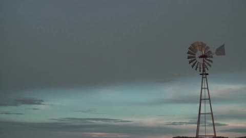 A car parked next to a large windmill in a field at sunset