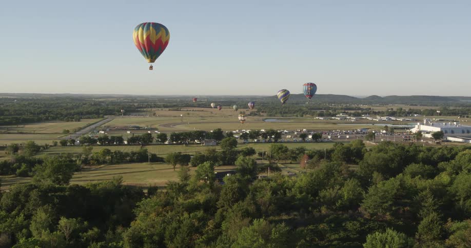 Hot air balloons floating over trees, fields and homes with mountain foothills in the background