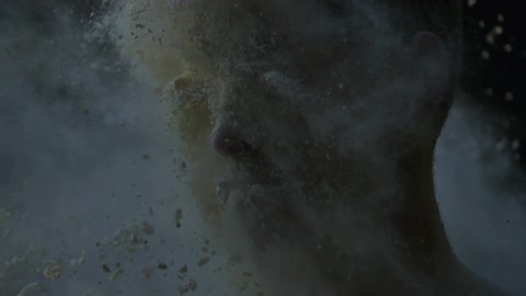 Slow motion footage of a large amount of a white, powdery substance hitting a man in the face and clinging to his skin