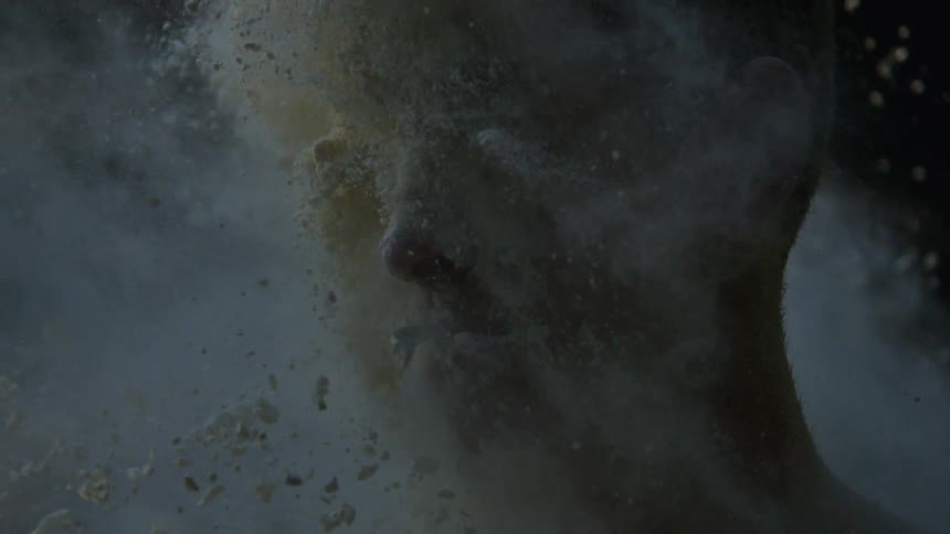 Slow motion footage of a large amount of a white, powdery substance hitting a man in the face and clinging to his skin