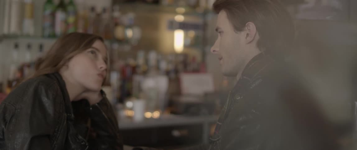 A woman sitting at a counter, smiling at a man and leaning her head on her hand