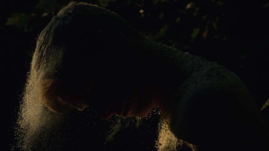 Silhouette of a young man shaking fine sand from his body in a dark room