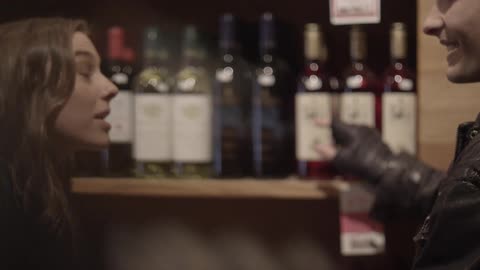 A young couple stand talking by wine bottles in a store