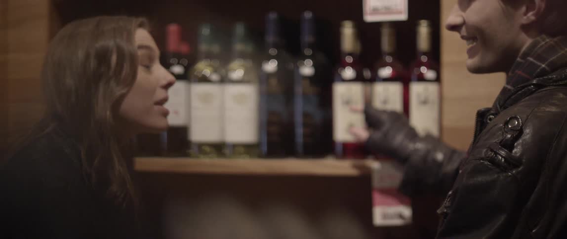 A young couple stand talking by wine bottles in a store