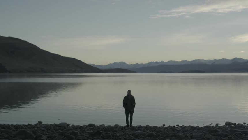 Man stands on rocky shore with back to lake