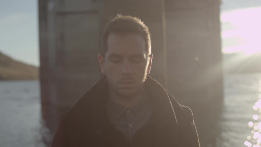 Man standing in front of water with his eyes closed