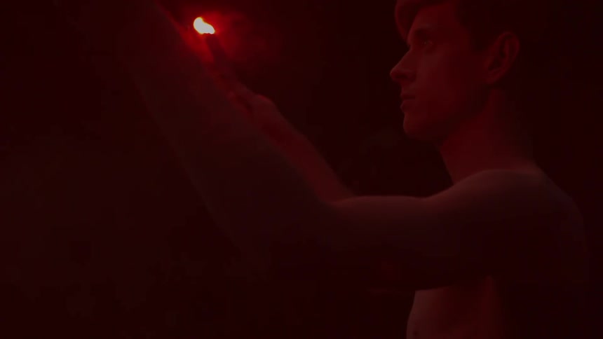 Shirtless young man holds flaming red emergency flares in his hands at night