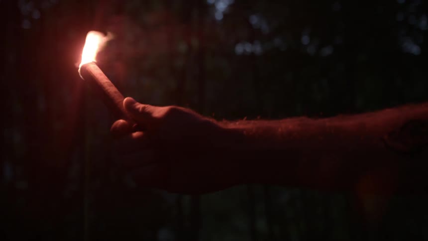 A man holds a flare in the dark