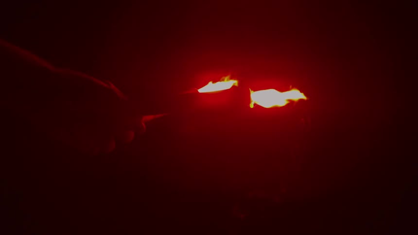 Person holding two flaming flares in the dark