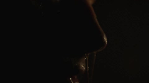 Water poured over mans face and dripping from his nose in a dark room