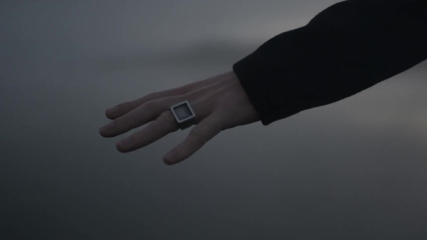 A person, wearing a square ring, stretching their hand out