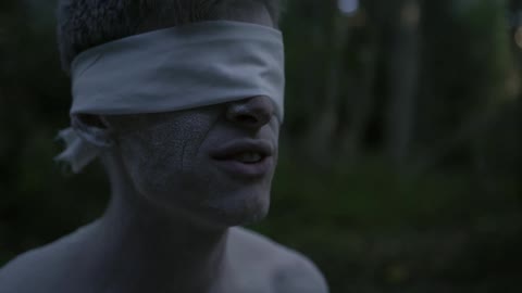 Blindfolded man talking in the woods