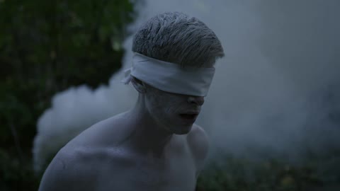Smoke billows behind a blindfolded man
