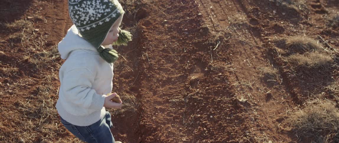 A toddler picks up dirt and tosses it into the air