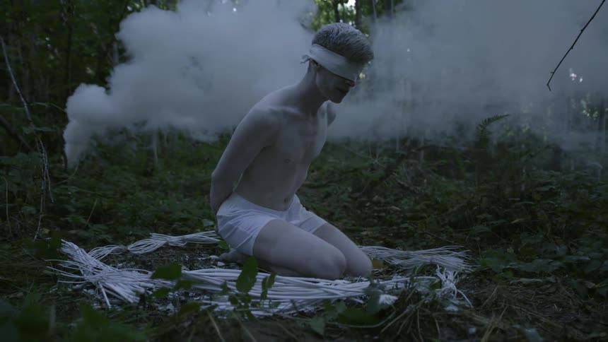 Smoke billows behind a blindfolded man in the woods