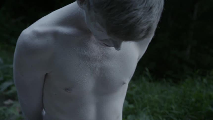 A very thin, very pale man with his arms behind his back and white powder on his skin