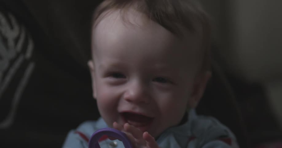 A baby smiling and putting a purple toy wrench in his mouth