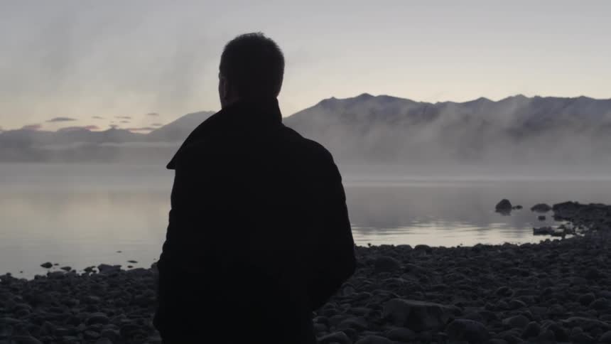 A man stands beside a misty body of water