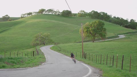 A bicyclist speeds down a hill on a curvy road